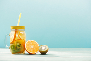 detox drink in jar with straw near orange and kiwi isolated on blue