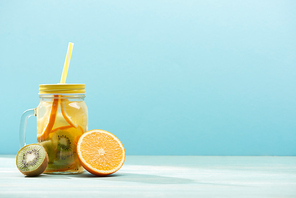 natural detox drink in jar with straw near orange and kiwi isolated on blue