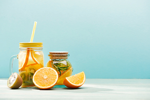 organic fruit detox drinks in jars near oranges and kiwi isolated on blue