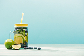 fresh detox drink in jar with straw near blueberries and limes isolated on blue