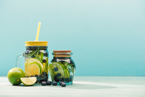 fresh detox drinks in jars near blueberries and limes isolated on blue