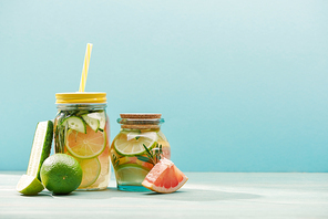 fresh detox drinks in jars near limes, cucumber and grapefruit isolated on blue