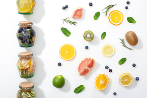 top view of detox drinks in jars near fruit slices, berries and herbs