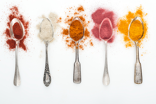 top view of various colorful spices in silver spoons on white background