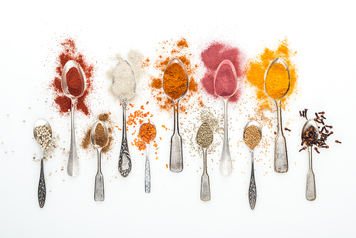 top view of various bright spices in silver spoons on white background