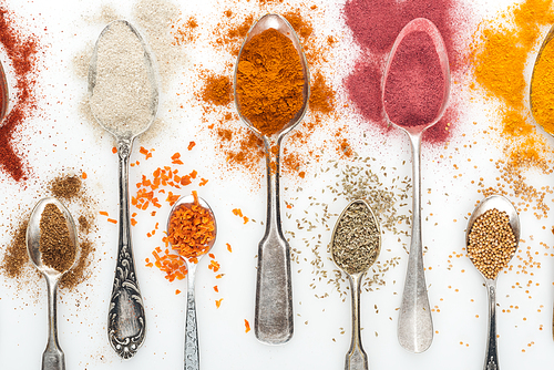 top view of various colorful spices in silver aged spoons on white background