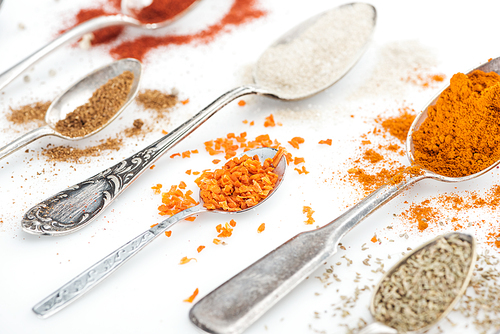 close up view of various colorful spices in silver spoons on white background