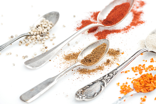 close up view of colorful spices in silver spoons on white background