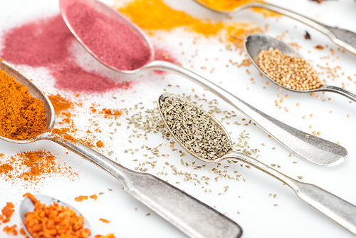 close up view of various aroma spices in silver spoons on white background