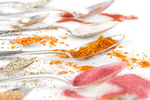 selective focus of colorful bright spices in silver spoons on white background