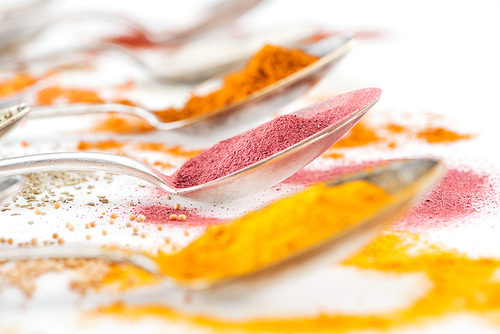 selective focus of colorful spices in silver spoons on white background