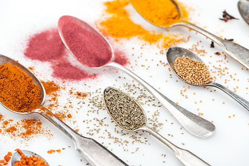 close up view of various spices in silver spoons on white background