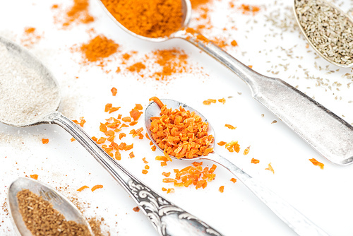 close up view of colorful spices in shiny spoons on white background
