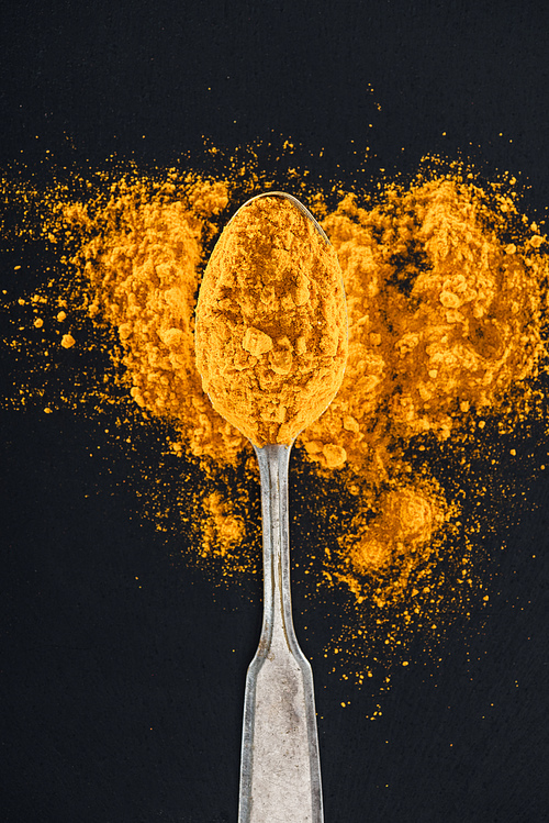 top view of curry powder in silver spoon on black background