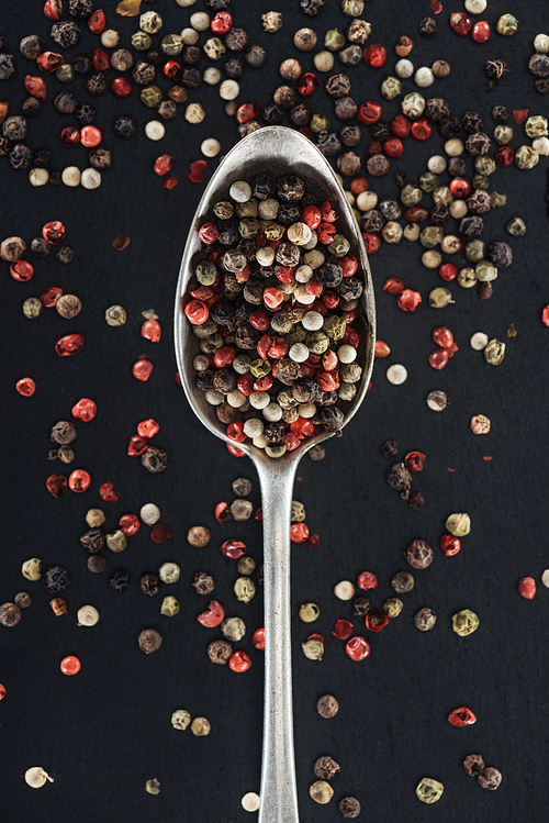top view of mix pepper spice in silver spoon on black background