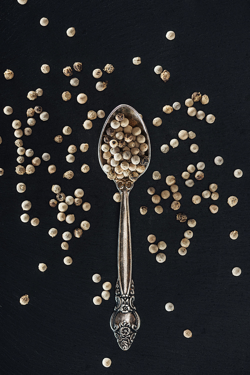 top view of white pepper in silver spoon on black background
