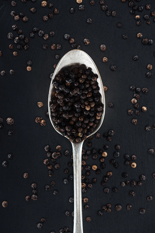 top view of black pepper in silver spoon on black background