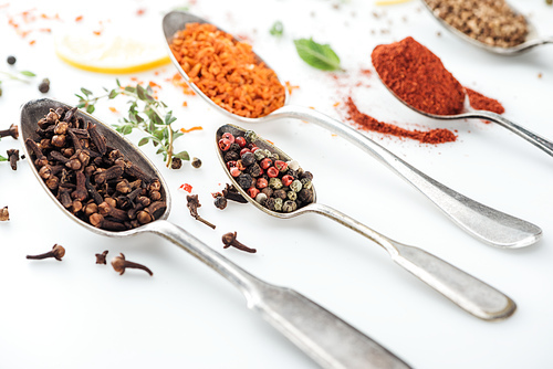 close up view of colorful indian spices in silver spoons on white background