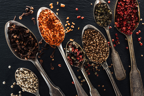 top view of indian spices in silver spoons on black textured background