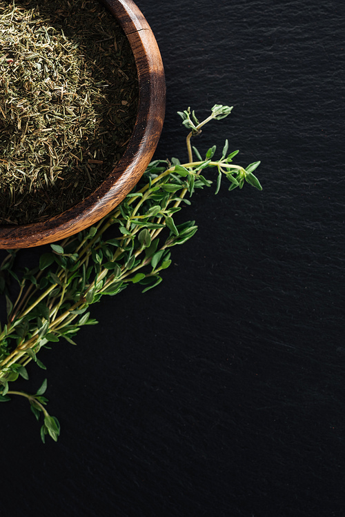 top view of dried thyme in wooden bowl near green herb on black background