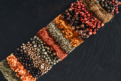top view of traditional bright indian spices and dried fruit on textured black background