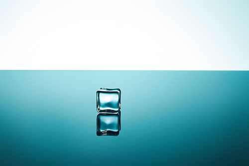 clear ice cube with reflection on emerald and white background