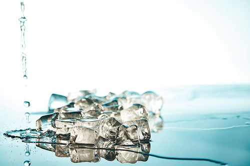 heap of transparent melted ice cubes with water puddles and drops  on emerald and white background