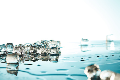 heap of transparent melted ice cubes with water puddles on emerald and white background