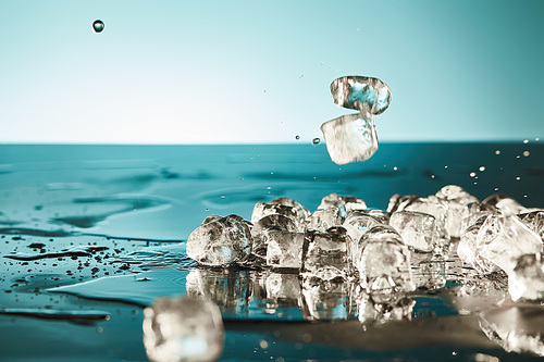 transparent melting ice cubes with puddles on emerald and white background