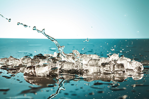 transparent melting ice cubes and water splash on emerald and white background