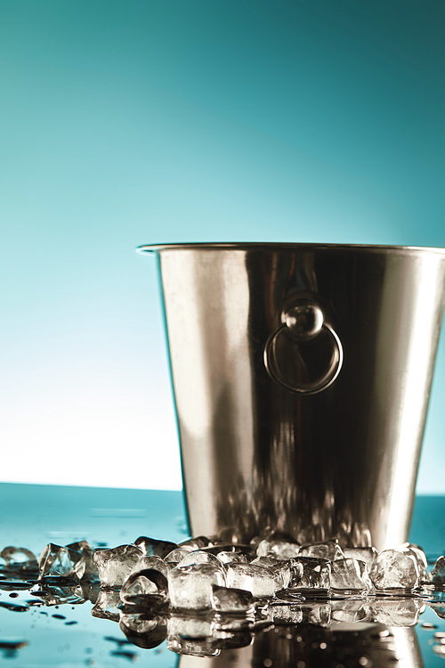 transparent ice cubes near metal bucket on emerald and white background