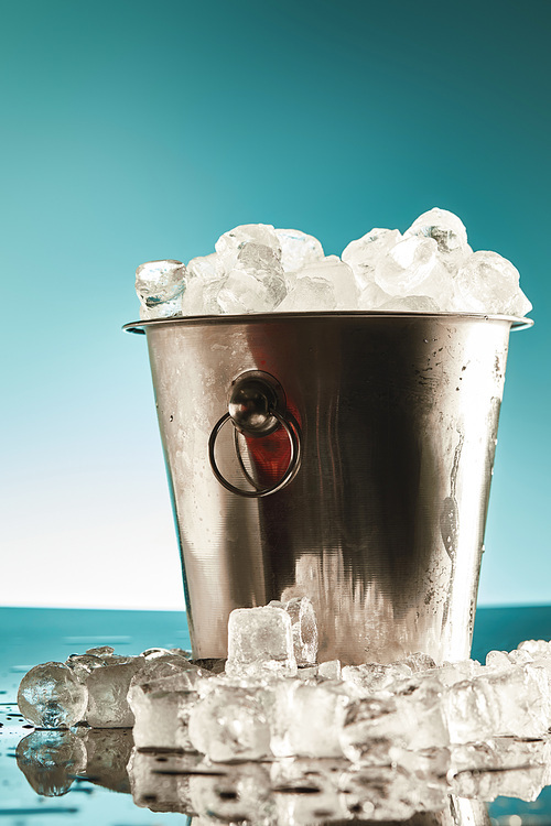 transparent ice cubes in metal bucket near water puddles on emerald and white background