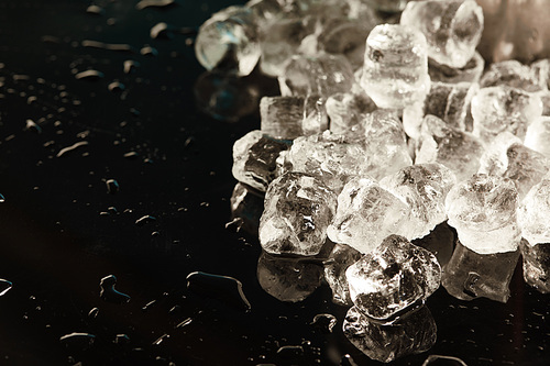 stack of transparent cool ice cubes on black background with water drops