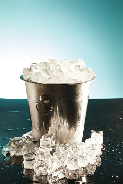 transparent ice cubes in metal bucket with water drops on surface on emerald and white background