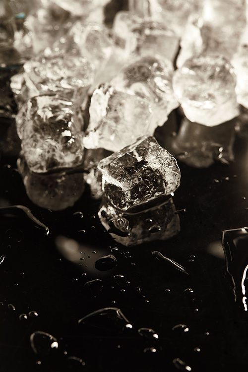 stack of transparent cool ice cubes on black background with drops