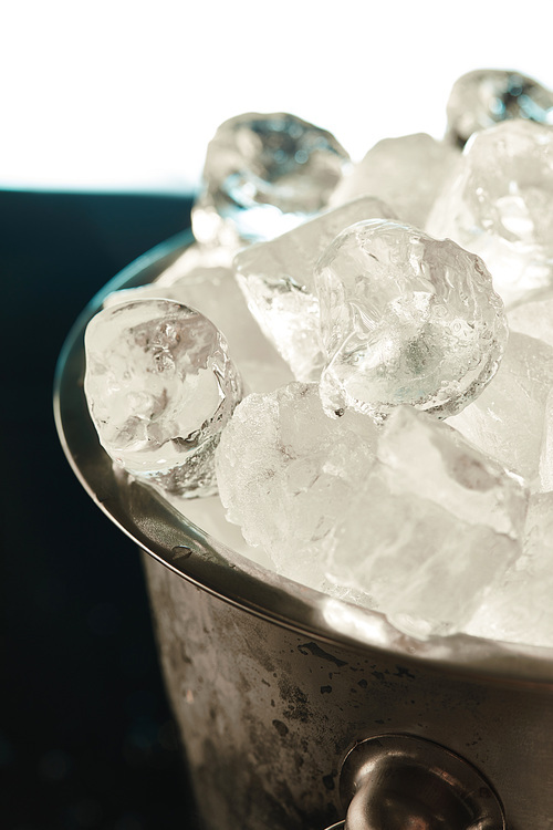 close up view of transparent ice cubes in metal bucket on emerald and white background