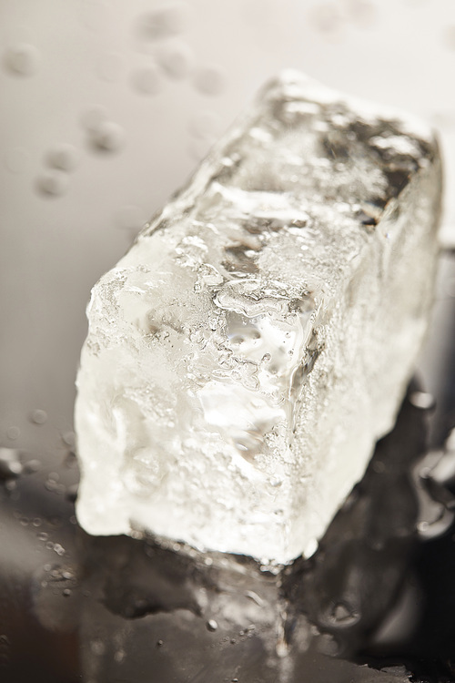 close up view of transparent wet textured ice cube on black background