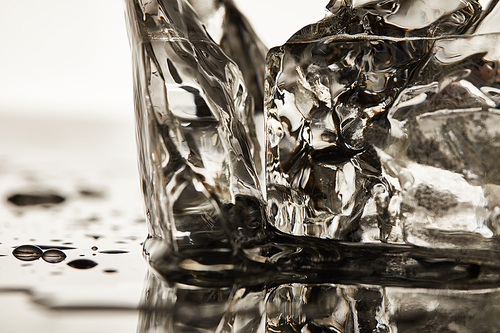 close up view of transparent melting ice cubes with puddles on white background