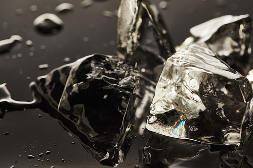 close up view of transparent melting ice cubes with drops on black background