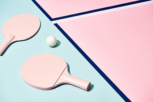 High angle view of ping pong rackets and ball on pastel surface with blue lines