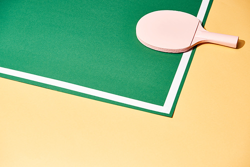 Wooden racket for table tennis on green and yellow background