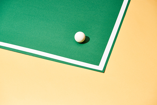 Table tennis ball with shadow on green and yellow background