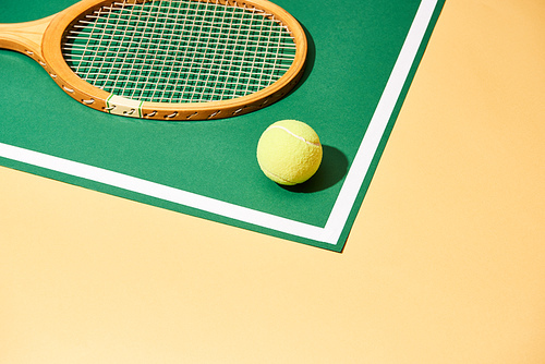 Tennis ball and wooden racket on green and yellow background