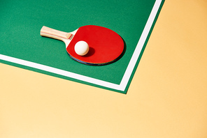 Wooden racket and ping pong ball on green and yellow surface
