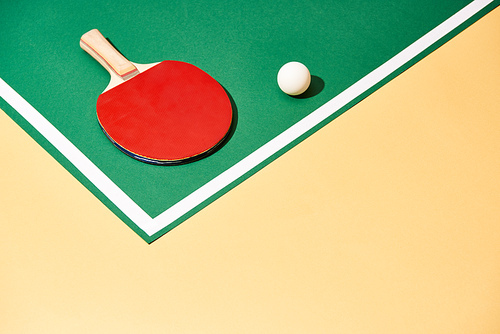 Table tennis racket and ball on green and yellow surface with white line