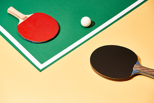 Two table tennis rackets and ball on green and yellow surface with white line