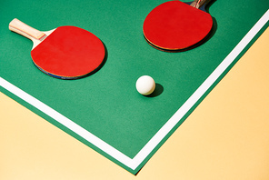 Red table tennis rackets and ball on green and yellow surface