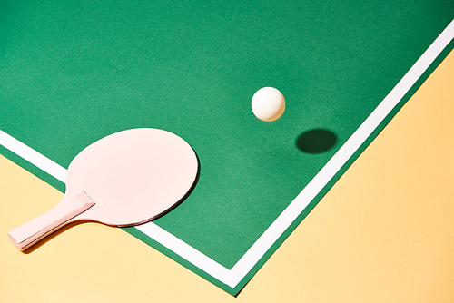 Table tennis racket and ball on green and yellow surface
