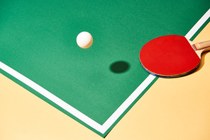 Red table tennis racket and ball on paying table and yellow surface