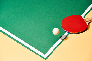 Ball and ping pong racket on yellow and green surface